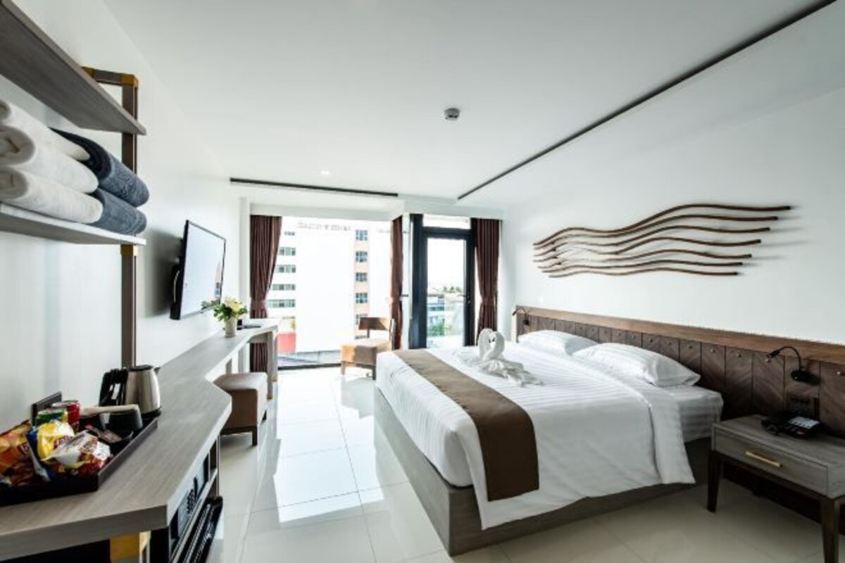 Ein Hotelzimmer mit Bett, Nachttisch, Schreibtisch mit Stuhl, Fernseher und Blick ins Freie.