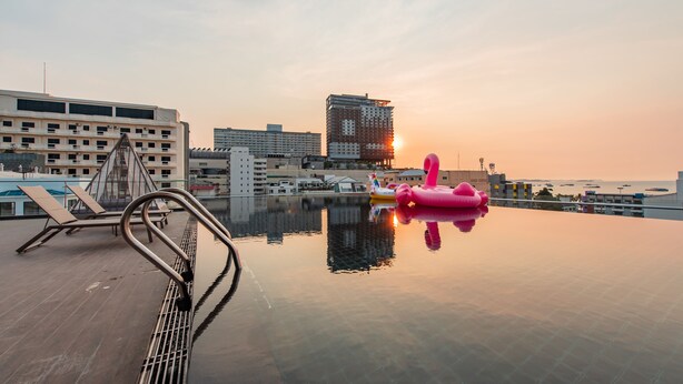 Zwembad op een dak met uitzicht over de stad, inclusief een hoog gebouw en een zonsondergang.