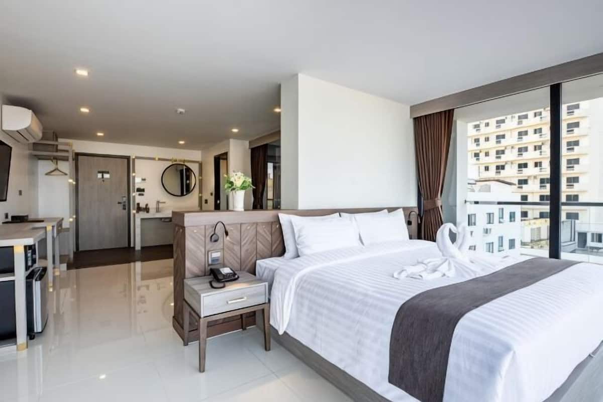 A hotel room with a bed, bedside table, lamp, and a view of the city.