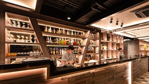 Een bar met houten planken vol flessen en glazen, een toonbank met een barman en een geruit vloertje.
