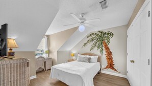 Een slaapkamer met een bed, een plafondventilator, een plant en uitzicht op het omliggende landschap.