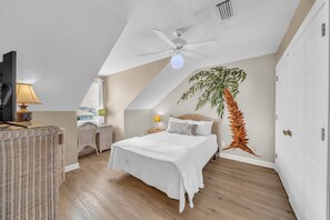 Una camera da letto con un letto, una ventola a soffitto, una pianta e vista sull'esterno.