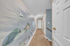 Un pasillo con un mural de criaturas marinas en la pared, suelo de madera y puertas blancas.