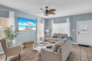 A living room with a sofa, armchairs, a coffee table, a ceiling fan, and a large window with blinds.