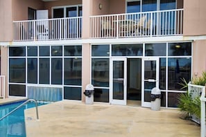 A hotel with a pool, a balcony, and a glass door entrance.