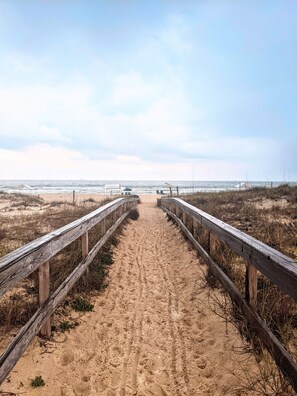 A sandy beach path with wooden railings, leading to the ocean.