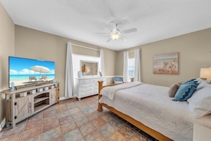 A bedroom with a bed, a TV, a dresser, and a ceiling fan.