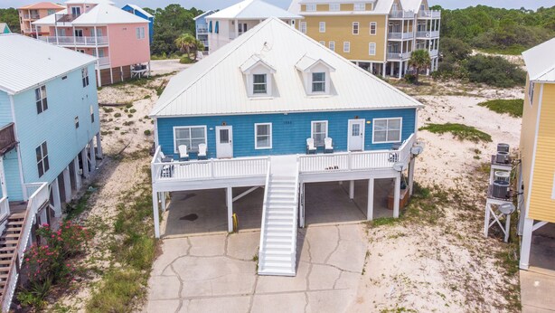 Een pand aan het strand met meerdere gebouwen, waaronder een opvallend blauw huis met een balkon en een witte trap naar de ingang.