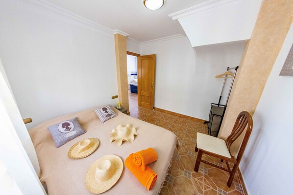 A hotel room with a bed, a chair, a wooden door, and a hallway leading to another room.