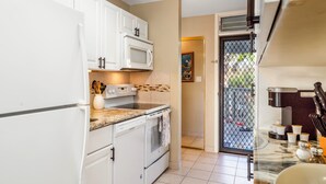 Cocina con armarios blancos, microondas, estufa y lavavajillas. Hay una puerta que da a un balcón con vistas al exterior.