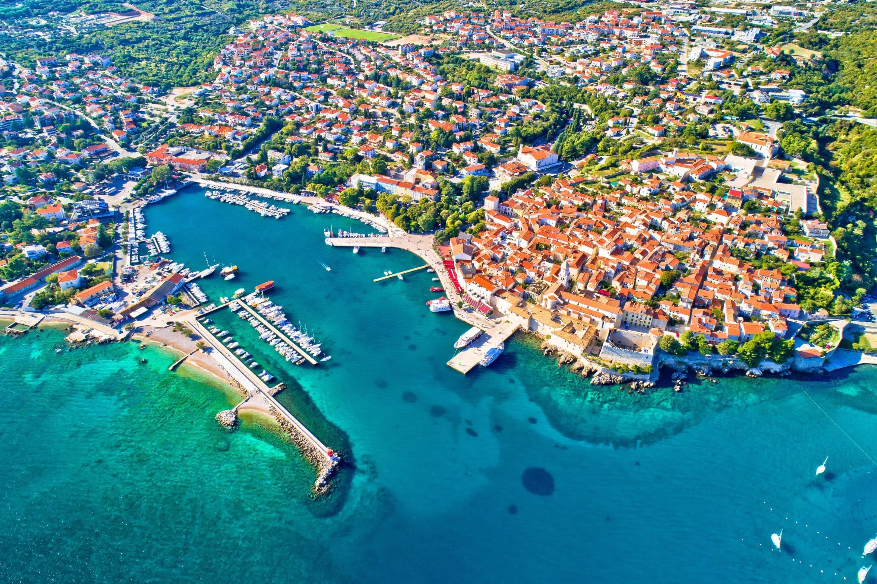 An aerial view of a coastal town with a marina, dense residential area, and a prominent castle-like structure.