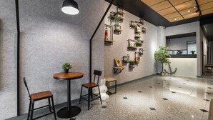 Un interior moderno con una pared de concreto pulido, una mesa de madera, dos sillas, una lámpara colgante y una escalera que lleva a un nivel superior.