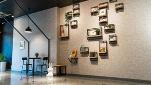 Un interior moderno con un diseño geométrico en la pared, estanterías empotradas con plantas y una zona de estar con sillas y una mesa.