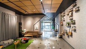 Un interior moderno con un sofá, una mesa de centro y una alfombra verde. Hay estanterías con plantas y marcos de fotos en la pared.