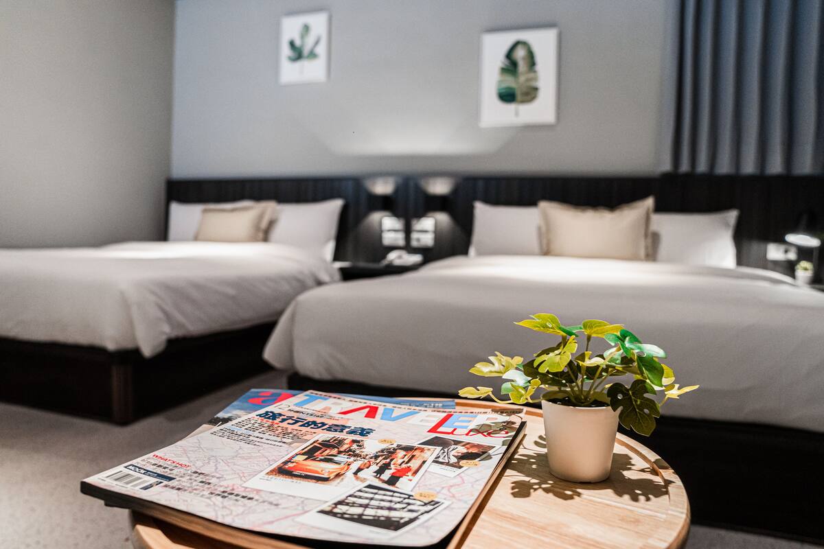 A hotel room with two beds, a magazine on a table, and a potted plant.