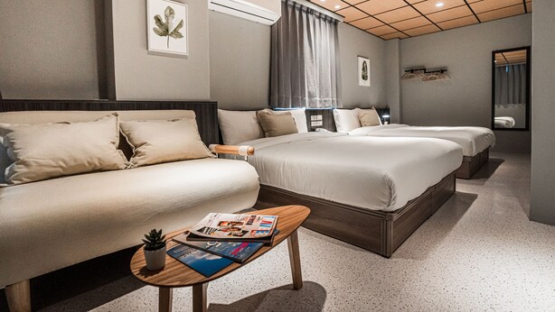 Una habitación de hotel con una cama grande, un sofá, una mesita con revistas, aire acondicionado y un espejo.