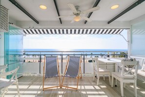 Ein Balkon mit Blick auf das Meer, einem Deckenventilator und einem Tisch mit Stühlen.