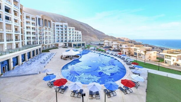 A hotel with a large pool featuring a floral design, outdoor seating with umbrellas, and a view of the sea. - Tolip Resort Elgalala Hills (Ataqah)