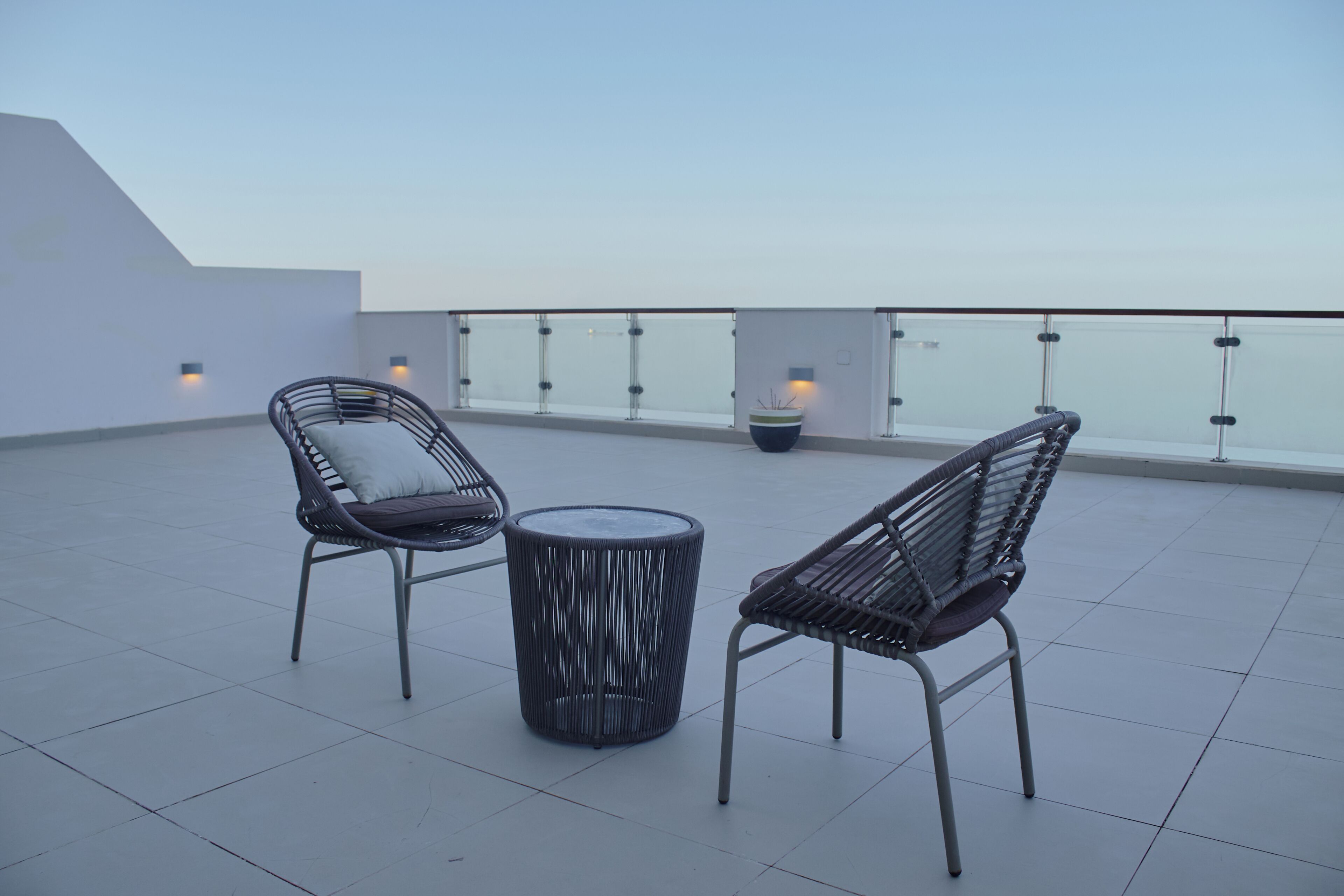 A rooftop terrace with two chairs and a round table, a railing, and a view of the sky.