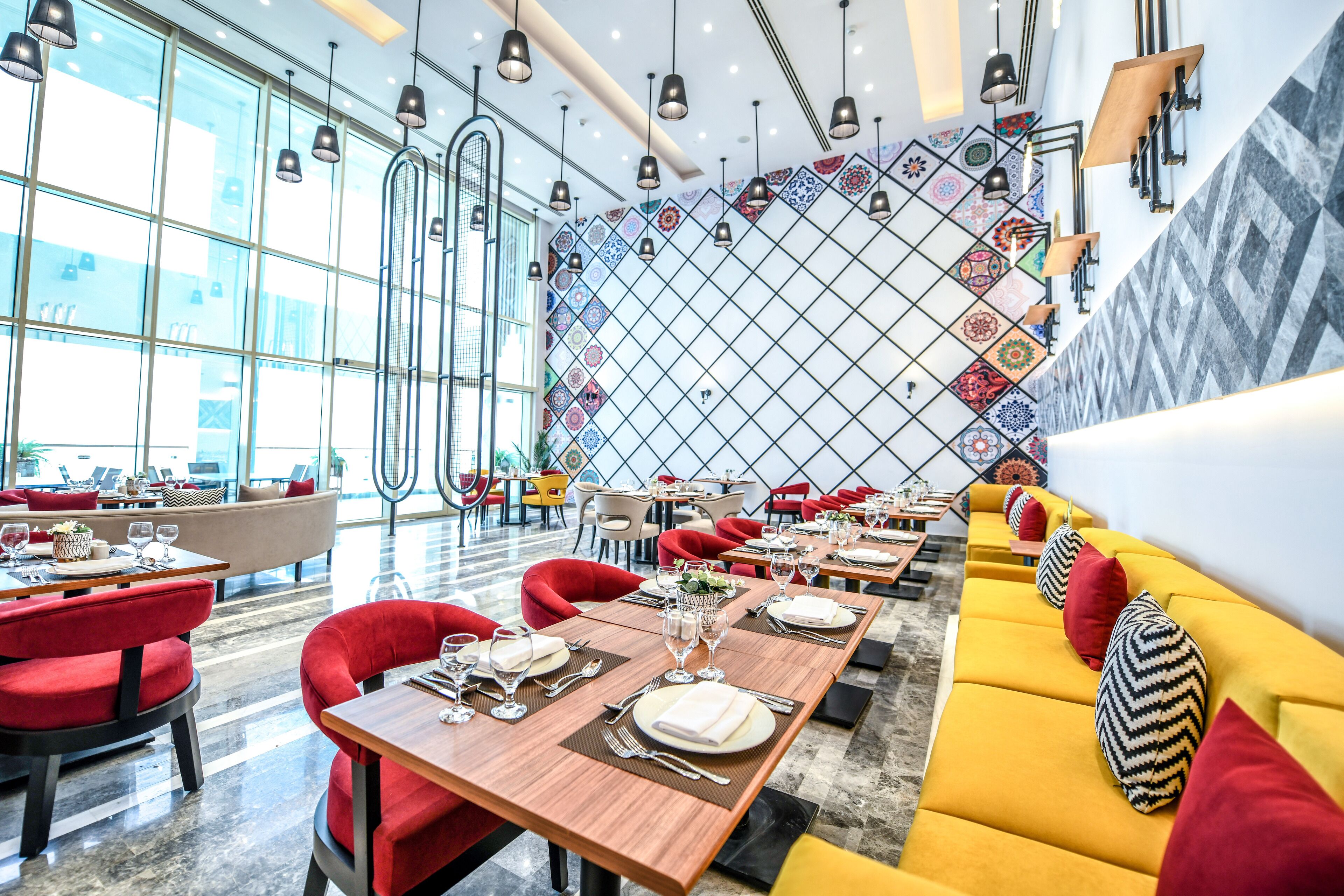 Um restaurante moderno com assentos vermelhos e amarelos, janelas amplas e azulejos de parede estampados.