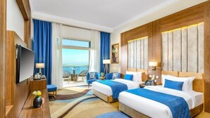 A hotel room with two beds, a TV, a desk, and a view of the sea. - Tolip Resort Elgalala Hills (Ataqah)