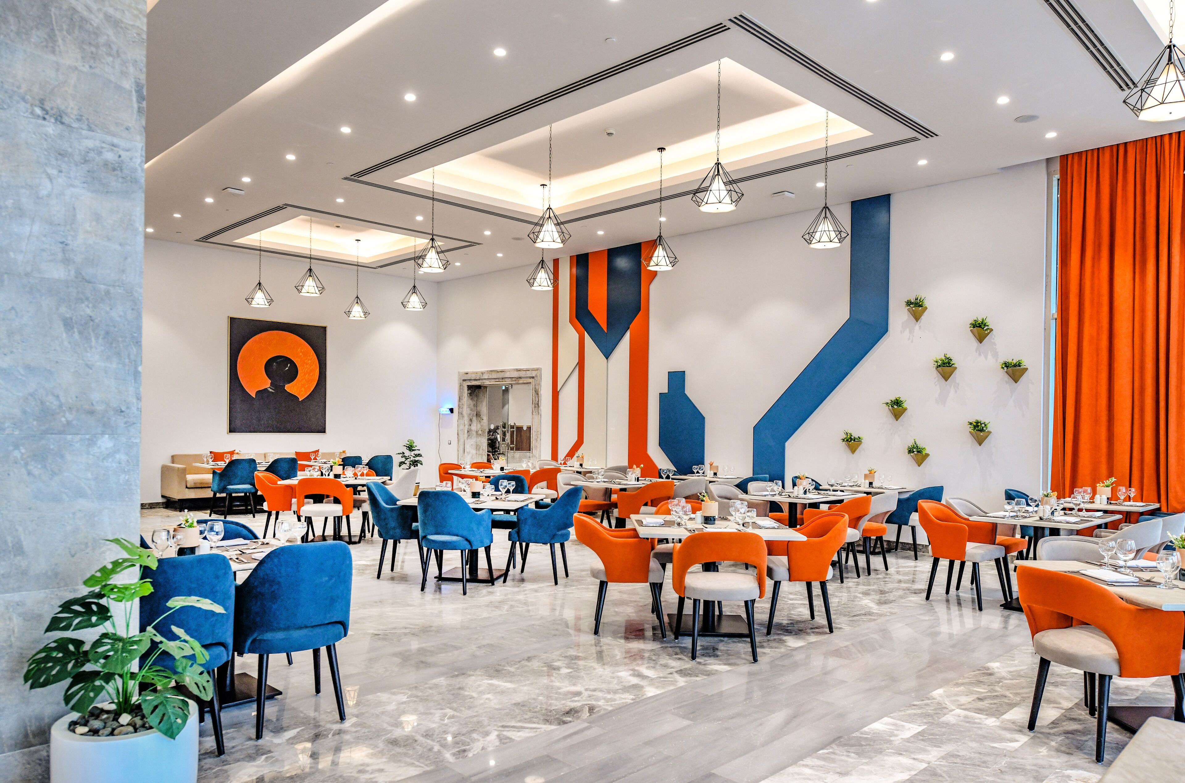A modern dining area with blue and orange chairs, a marble floor, and pendant lighting.