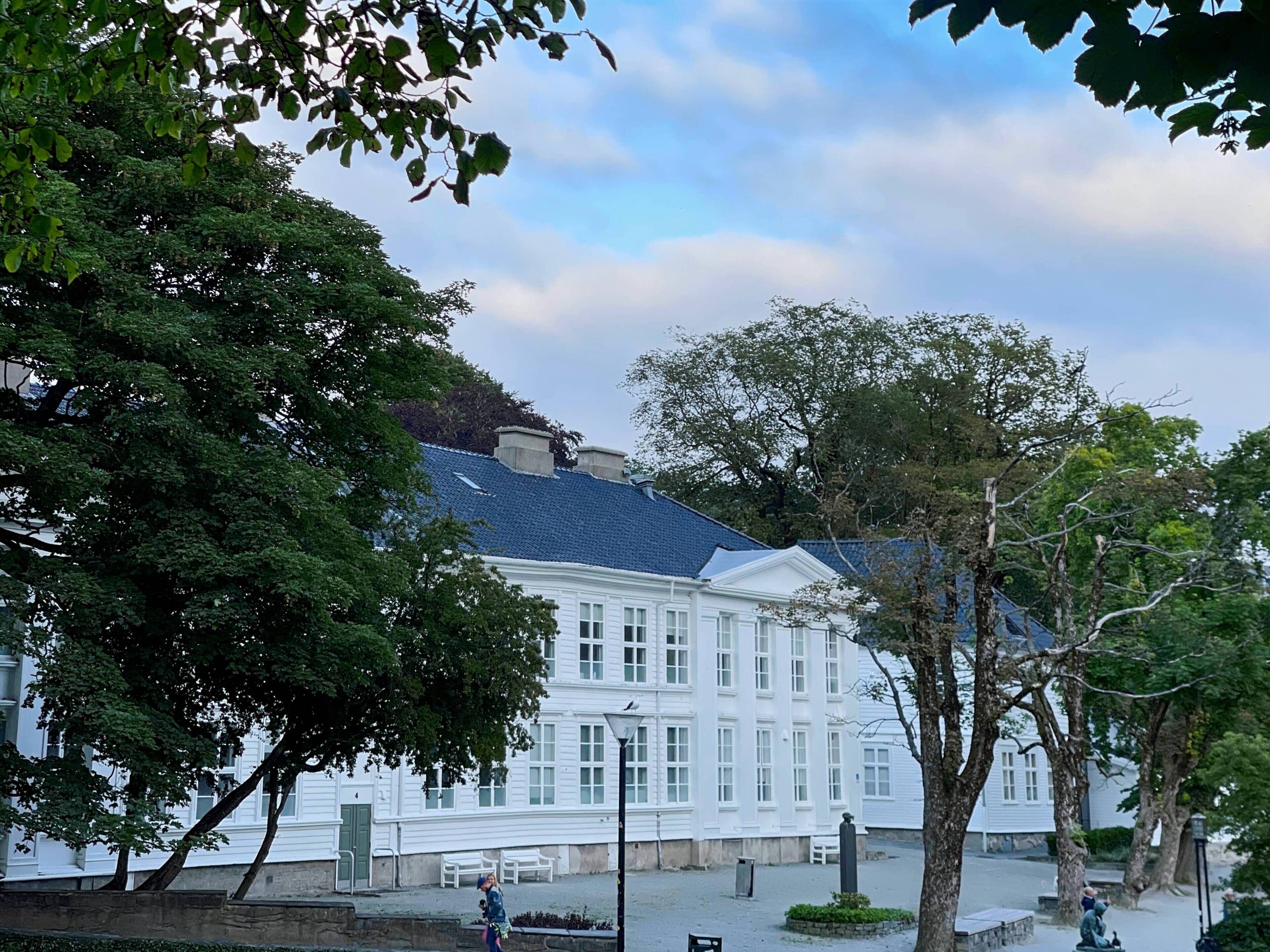A white building with a blue roof, surrounded by trees and benches.