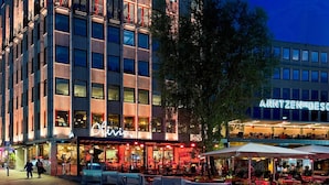 Un edificio de varios pisos con un restaurante llamado 'Olivia' en la planta baja, mesas al aire libre y un letrero de 'ARNTZENDEBES' en el nivel superior.
