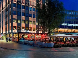 A multi-story building with a restaurant named 'Olivia' on the ground floor, outdoor seating, and a sign for 'ARNTZENDEBES' on the upper level.