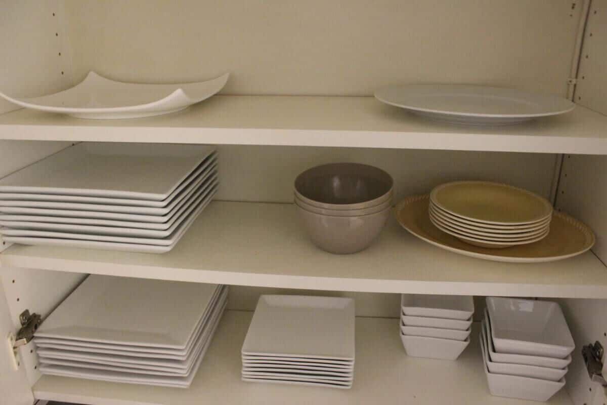 A storage unit with shelves containing stacks of white plates, bowls, and a few decorative plates.