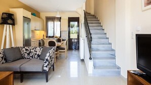Una sala moderna con sofá, televisor y escalera que lleva a una zona de cocina.