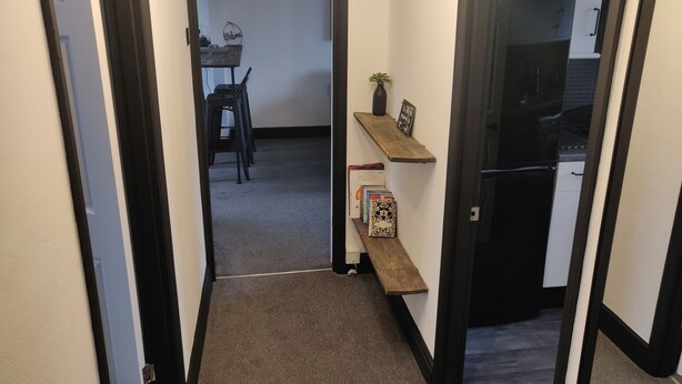 A narrow hallway with a carpeted floor, a wooden bench, a small shelf with books, and a 'Welcome' sign. - 1 Bedroom Riverside Apartment St Neots Riverside Park Area (St Neots)