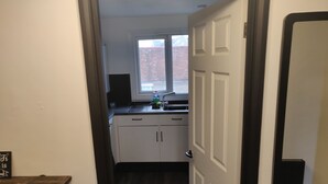 A narrow hallway leading to a kitchen with white cabinets, a window, and a door. - 1 Bedroom Riverside Apartment St Neots Riverside Park Area (St Neots)