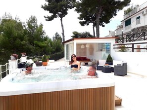 A hot tub with three people, surrounded by outdoor furniture and a glass-enclosed lounge area. - Residence Maresol Two-bedroom Villa With Terrace Sea View (Vieste)