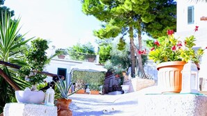 A courtyard with potted plants, a stone bench, and a dog lying on the ground. - Residence Maresol 1 Bedroom Apartment (Vieste)