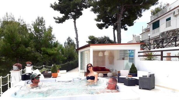 A hot tub with three people, surrounded by outdoor furniture and a glass-enclosed lounge area. - Residence Maresol 1 Bedroom Apartment (Vieste)