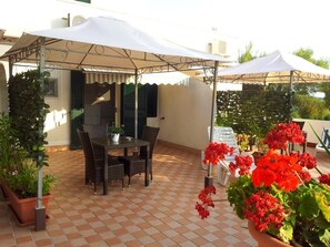 An outdoor patio with a table and chairs, surrounded by potted plants and red flowers. - Residence Maresol Studio Apartment With Sea View (Vieste)