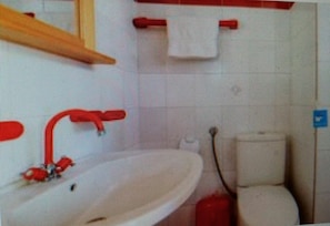 A bathroom with a white sink, red faucet, and a toilet.