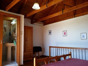 A wooden-framed room with a bed, a wooden cabinet, and a bathroom visible through an open door. - S West Crete Cottage (Kantanos-Selino)