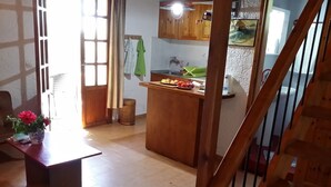 A kitchen with wooden cabinets, a central island with fruits, a sink, and a window with curtains.