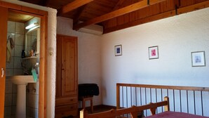 A bedroom with a wooden bed, a wooden chair, a wooden wardrobe, a bathroom with a sink and mirror, and a ceiling with wooden beams.