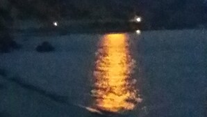 A nighttime scene with a full moon reflecting on a body of water, surrounded by hills.