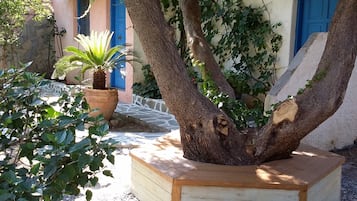 A tree with a wooden planter box, a stone wall, and a building with blue doors.