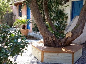 A tree with a wooden planter box, a stone wall, and a building with blue doors. - Exclusive Cottages are in S West Crete in a Quiet Olive Grove Near the sea (Kantanos-Selino)