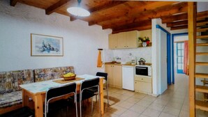 A cozy kitchen with wooden cabinets, a dining area with a table and chairs, and a staircase leading to an upper level. - Exclusive Cottages are in S West Crete in a Quiet Olive Grove Near the sea (Kantanos-Selino)