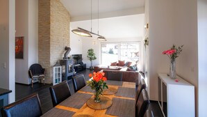 A modern dining area with a wooden table, woven placemats, and a vase of flowers. There is a stone accent wall and a view of the living area in the background. - Modern and Cosy 5 Rooms Penthouse With Stunning View (Triesenberg)