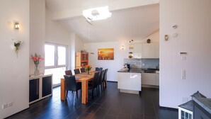 A modern kitchen with white cabinets, a dining area with a wooden table and chairs, and a large window providing natural light. - Modern and Cosy 5 Rooms Penthouse With Stunning View (Triesenberg)