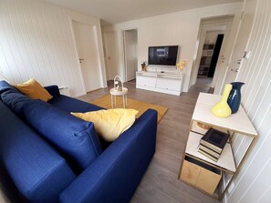 A living room with a blue sofa, a small white side table, a flat-screen TV, and a bookshelf. - Central Trio Suites by Stavanger BnB Nr 5 (Stavanger)