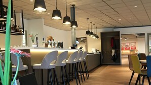 A modern bar area with high stools, pendant lighting, and a counter with a bartender. - Northseachalets Ameland (Buren)