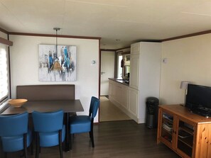 A compact kitchen with a refrigerator, a dining table with chairs, and a television on a wooden cabinet.